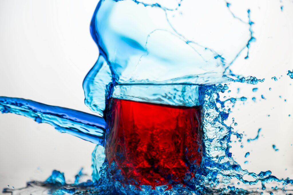 Dynamic shot of red liquid in glass colliding with blue water splash.