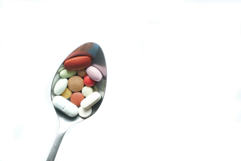 A variety of colorful pills and tablets resting on a spoon on a white background.