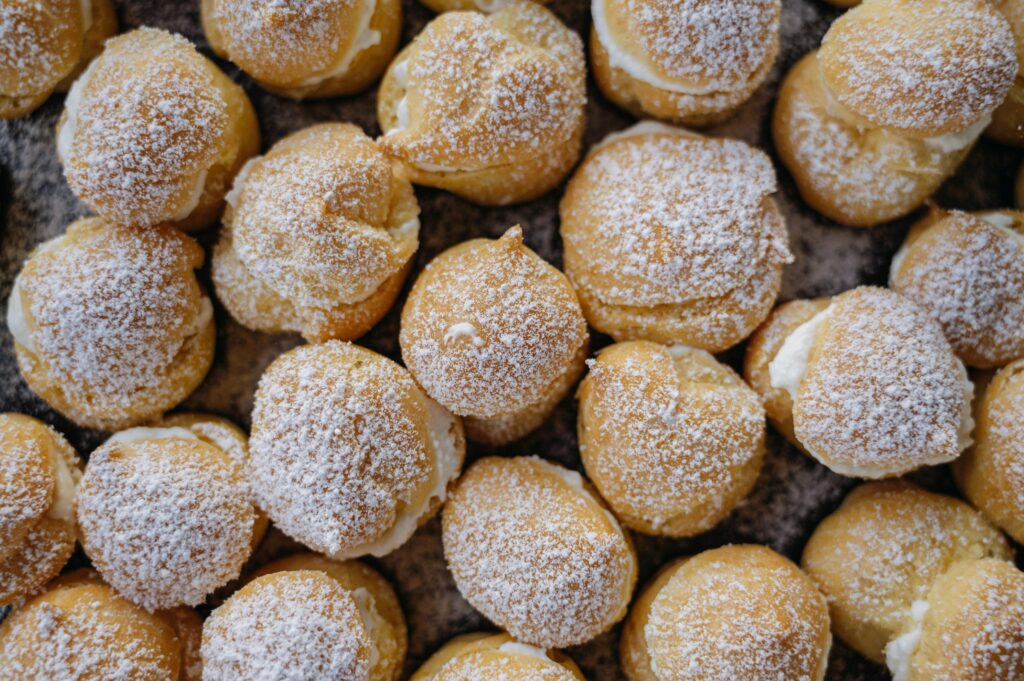 Freshly baked cream puffs topped with powdered sugar, showcasing a delightful dessert arrangement.