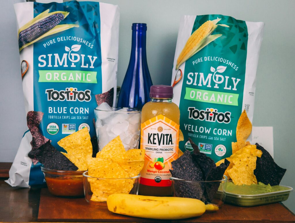 A colorful assortment of organic snacks including Tostitos chips and Kevita drink.