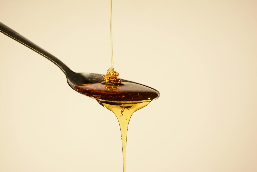 Close-up of golden honey flowing from a spoon against a soft yellow backdrop, capturing its sweet allure.