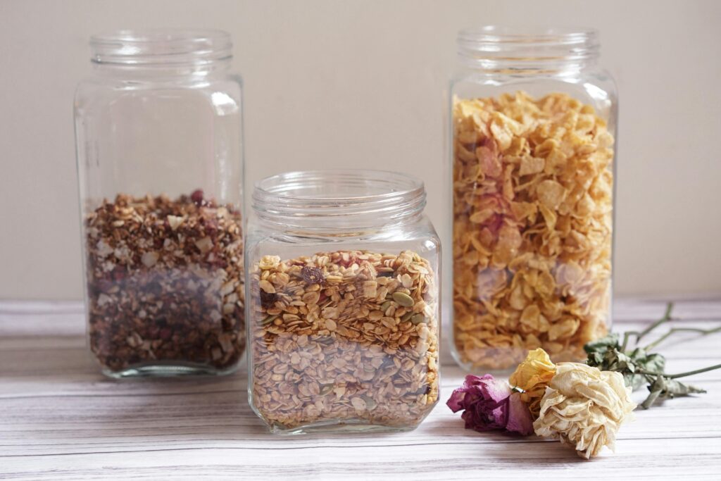 Three clear jars filled with cereal, granola, and flowers on a wooden surface in natural light.