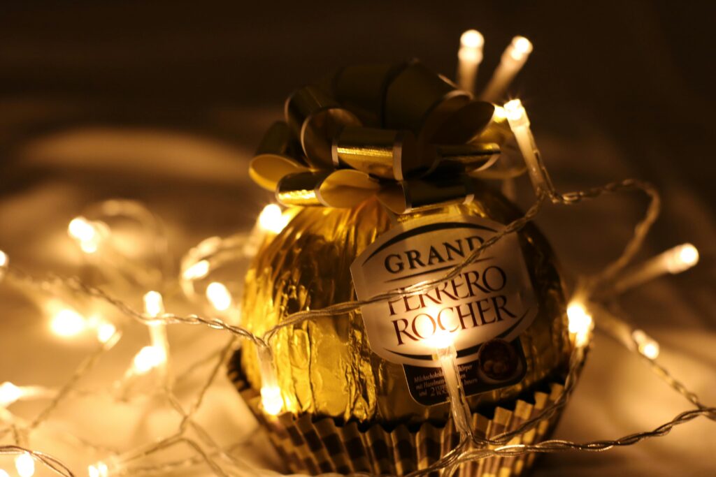 A Grand Ferrero Rocher chocolate illuminated by warm LED string lights, perfect for Christmas decor.