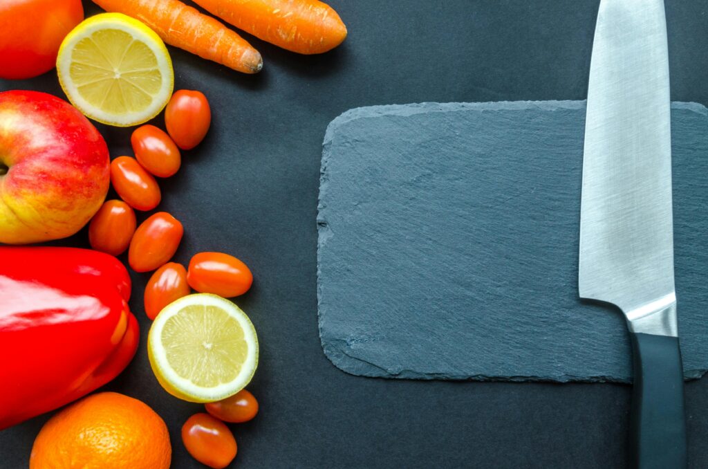 Vibrant fruits and vegetables with a stainless steel knife on slate, perfect for healthy eating concepts.